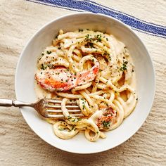 a white bowl filled with pasta and shrimp on top of a blue and white table cloth