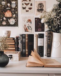 a white desk topped with lots of books and vases filled with flowers on top of it