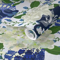 a blue and white floral wallpaper with flowers on the bottom half of it, next to a roll of toilet paper