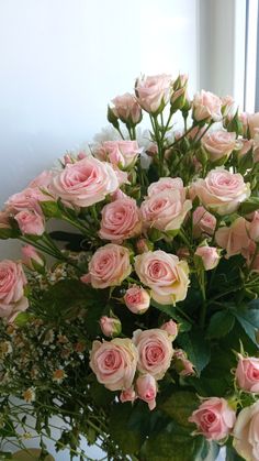 a vase filled with lots of pink roses on top of a table next to a window