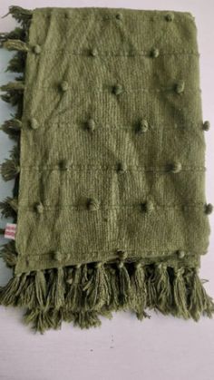 a green scarf with fringes and buttons on the ends is laying on a white surface