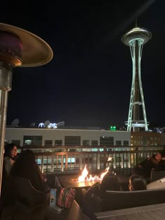 people sitting around a fire pit with the space needle in the background