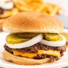 a cheeseburger with pickles and onions on a plate next to french fries