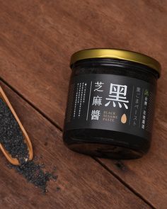 an open jar of black sesame seeds next to a spoon on a wooden surface with chinese writing