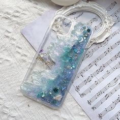 a phone case with blue and green glitters on it sitting next to music sheets