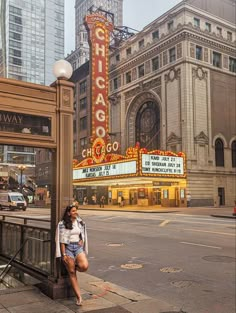 a woman sitting on the side of a street next to a theater marquee