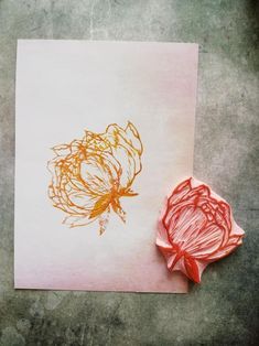 a piece of paper with an orange flower drawn on it next to a wax block