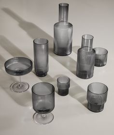 a group of glass vases and glasses on a white table with shadows from them