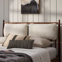 a bed with white sheets and pillows in a bedroom next to a painting on the wall