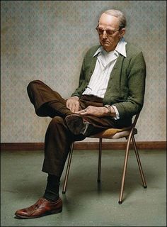 an old man sitting in a chair with his legs crossed and looking at the camera