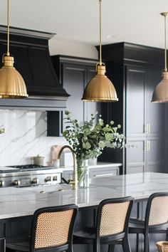 a kitchen with black cabinets and gold pendant lights