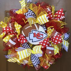 a football wreath is hanging on the front door with red, yellow and white bows