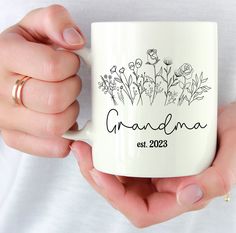 a woman holding a white coffee mug with flowers on it