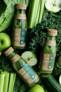 several bottles of green juice surrounded by vegetables