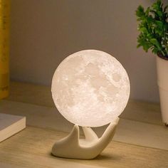 the moon lamp is sitting on a table next to a potted plant