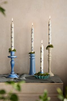 four candles are sitting on a table with blue vases and greenery in front of them