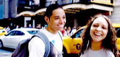 a man and woman walking down the street in new york city, with taxi cabs behind them