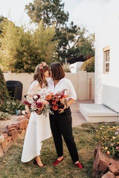 two women standing next to each other in front of a house with flowers on their heads