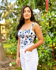 a beautiful young woman standing in front of a tree wearing white pants and a floral top