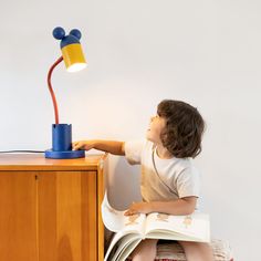 a little boy sitting on a chair reading a book with a lamp on top of it