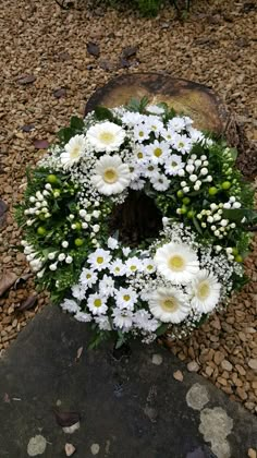 a wreath with daisies and other flowers is placed on the ground next to a rock