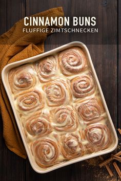 cinnamon buns in a baking pan on top of a wooden table with cinnamon sticks