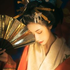 a geisha woman in traditional japanese dress holding a fan and looking down at her face