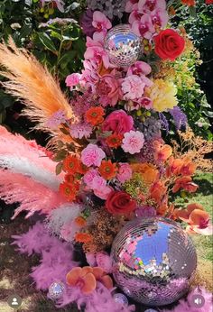 an arrangement of flowers, feathers and disco ball in the middle of a garden area