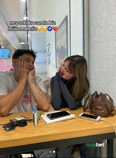 a man and woman sitting at a table with their hands covering their faces while looking at the camera