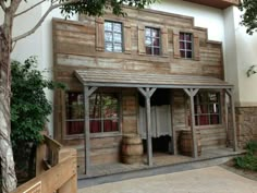 an old wooden building with two barrels in front of it and trees around the entrance