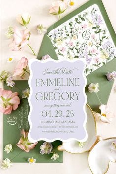 the wedding stationery is surrounded by flowers and greenery, including green envelopes