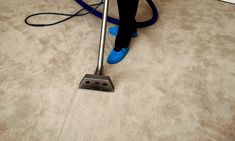 a person using a vacuum to clean the floor in a room with white walls and carpet