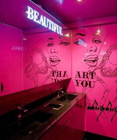 a bathroom with pink walls and graffiti on the wall, along with a sink in front of it