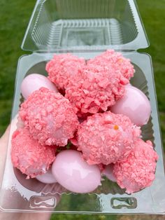 pink cake balls are in a clear plastic container with green grass behind them and someone holding it