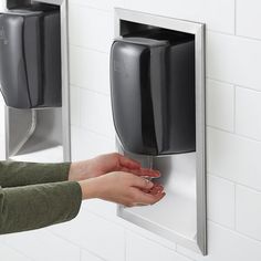 a woman's hand is holding onto the wall mounted soap dispenser