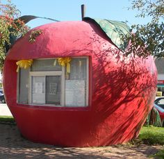 a large red apple shaped building sitting on the side of a road next to a tree