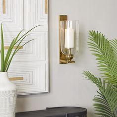 a white vase sitting on top of a table next to a wall mounted candle holder