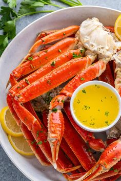 a white plate topped with crab legs and lemon wedges next to a bowl of dipping sauce