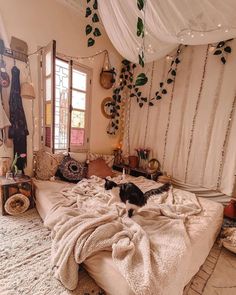 a cat sitting on top of a bed in a room with lots of pillows and blankets