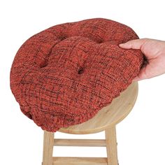 a hand is holding the seat cushion on top of a stool with a wooden base