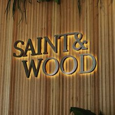 the sign for saint and wood is lit up against a wooden wall with plants on it