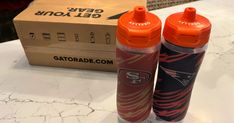 two orange sports bottles sitting on top of a table next to a box and some scissors