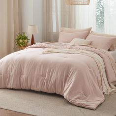 a bed with pink comforter and pillows in a room next to a white window