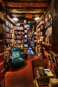 a room filled with lots of books next to a green chair and bookcases