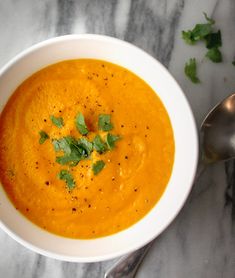 a white bowl filled with carrot soup and garnished with cilantro