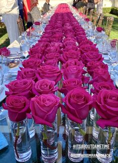 the long table is lined with clear vases filled with pink roses