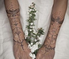 two hands with tattoos and flowers on their palms, both holding each other's arms