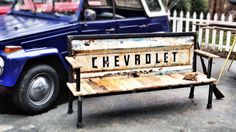 an old blue pickup truck parked next to a wooden bench with the word chevrolet painted on it