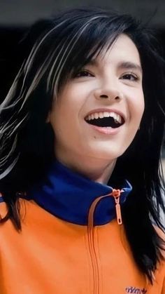 a woman with long black hair smiling and wearing an orange jacket