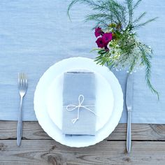 a place setting with napkins, silverware and flowers on a wooden table top